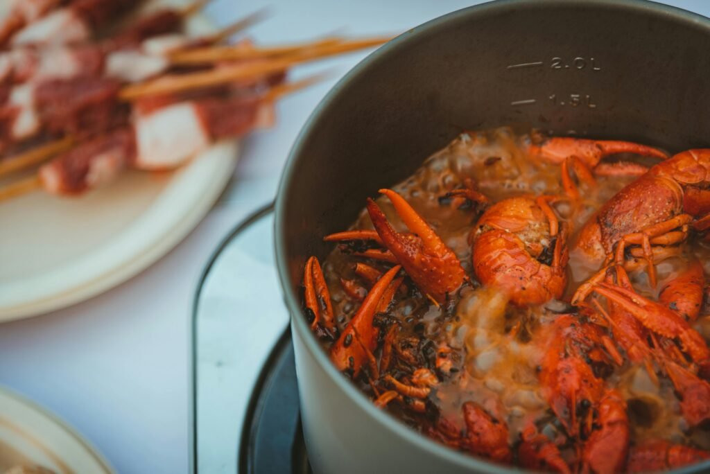 A large pot of seafood boil cooking on a high-power outdoor burner, with friends and family gathered around on a sunny patio, ready to eat.