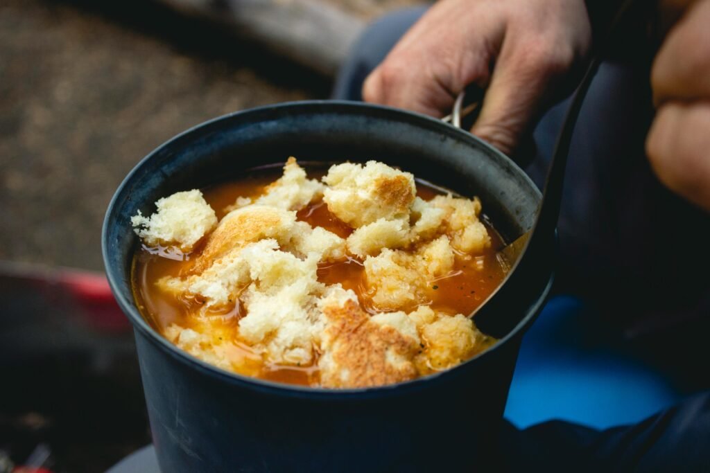 A close-up of a delicious and easy one-pot meal cooking in a cast-iron skillet over a vibrant campfire, representing the best food for camping.