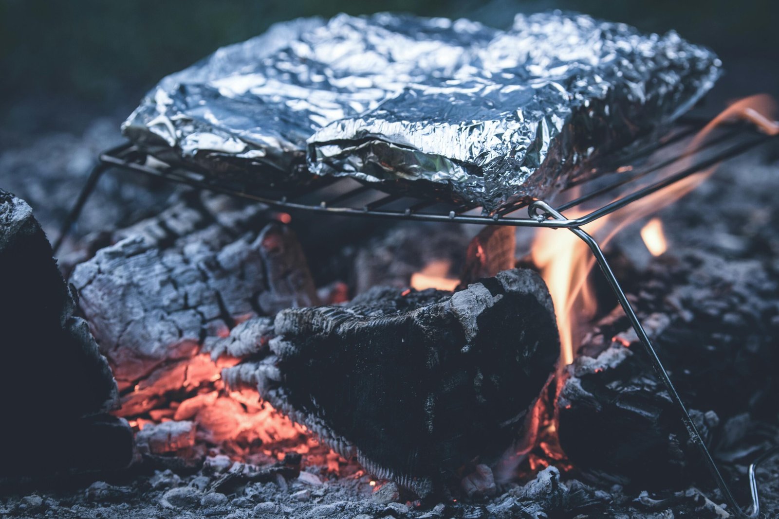 A close-up of a pie iron cooking a perfectly golden, sealed sandwich over a flickering campfire, showcasing easy and delicious camping recipes and outdoor meals.