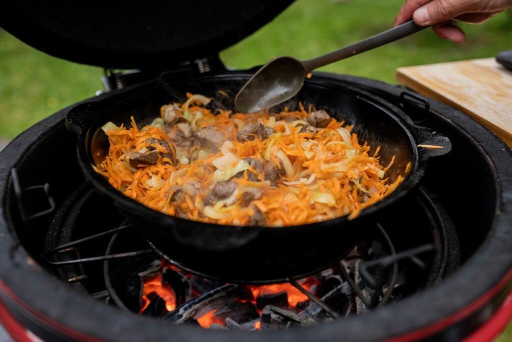 A person preparing one of several healthy camping meals by cooking colorful, fresh vegetables in a pan on a camp stove with a blurred forest background.