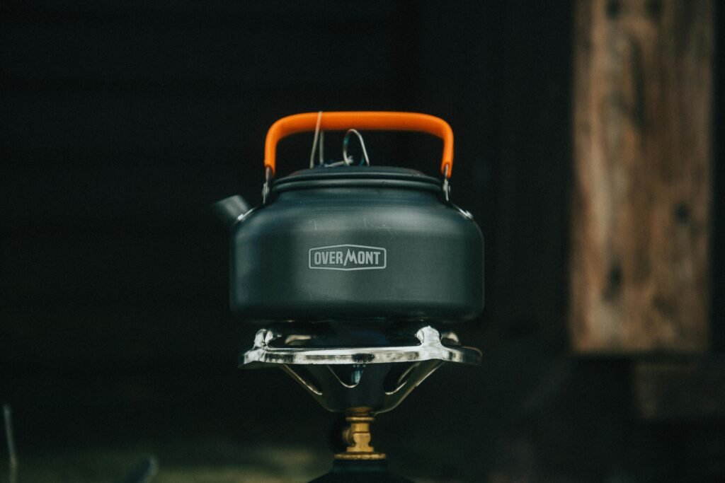 A portable outdoor stove burner with a pot of food cooking on it, set up on the ground in a beautiful forest setting.