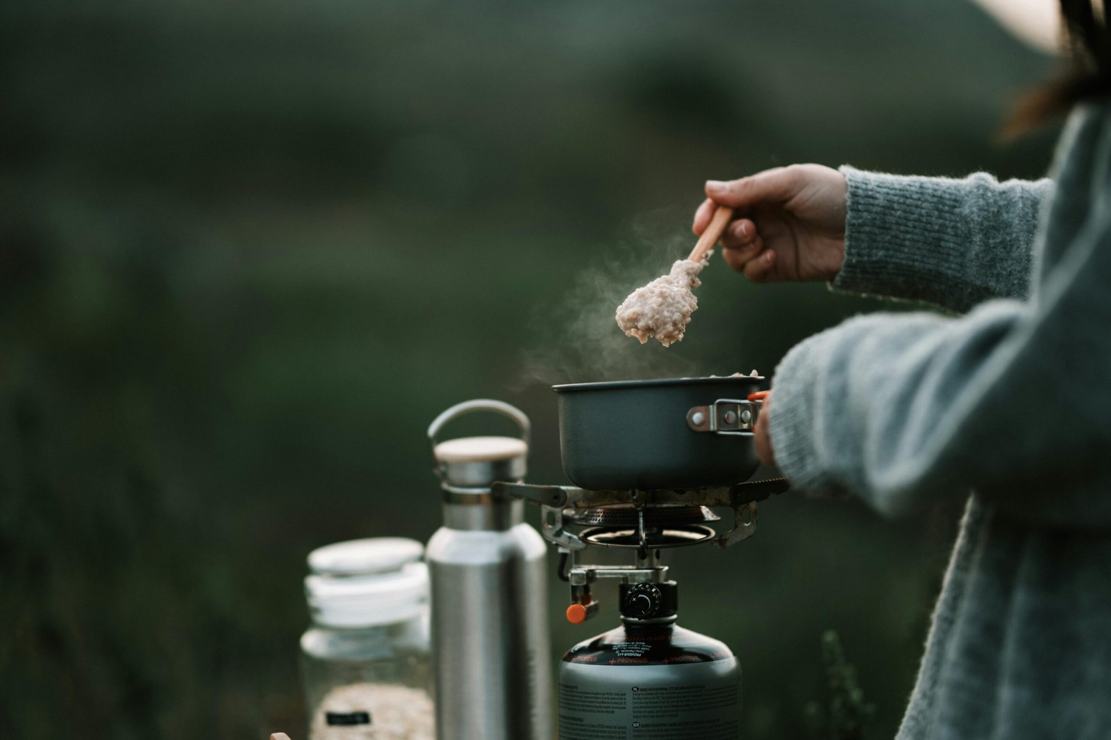Portable dual-fuel butane propane stove efficiently cooking a meal at a scenic campsite, highlighting its versatility and reliability for outdoor adventures and emergency preparedness.