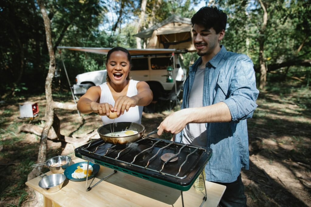 A smiling couple preparing a simple one-pot meal on a camp stove, an example of easy camping food for a stress-free outdoor adventure.
