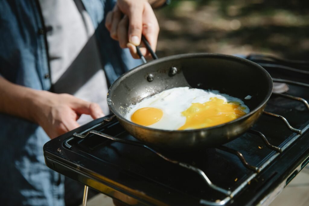 A person cooking on a compact portable single burner stove during a camping trip, demonstrating a convenient cooking solution for outdoor adventures and small spaces.