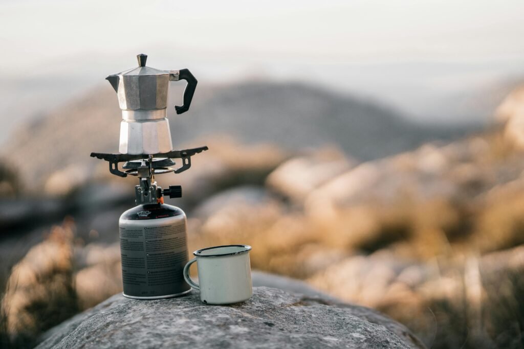 Close-up of a modern camp stove boiling water for coffee amidst a scenic outdoor camping backdrop, highlighting essential gear for reliable outdoor cooking and memorable camping trips.