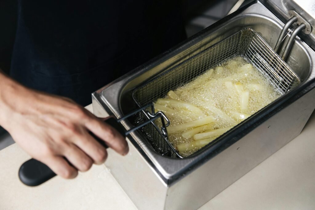 A close-up shot of a metal basket filled with perfectly golden and crispy french fries being lifted out of a modern Ninja deep fryer.