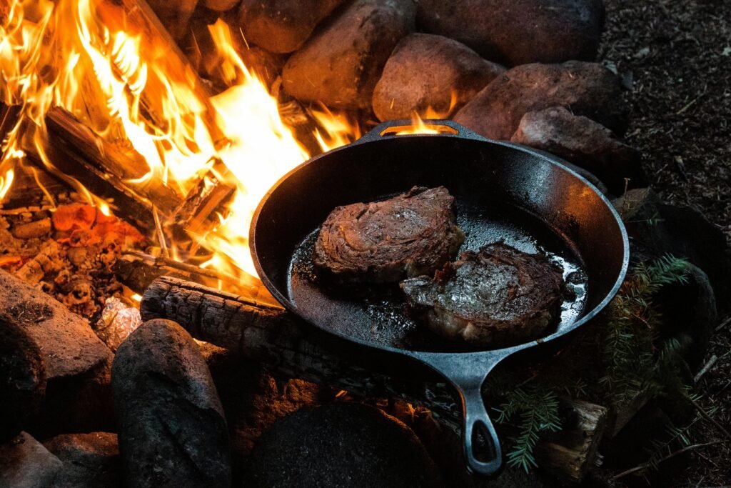 A close-up of one of the best camping meals sizzling in a cast-iron skillet, placed over the hot embers of a campfire for easy cooking.