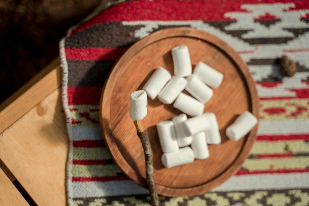A delicious spread of camping snacks, including trail mix and s'mores ingredients, laid out on a log next to a glowing campfire.