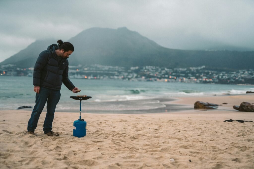 A person cooking a meal on a portable gas hob in a scenic outdoor campsite, emphasizing its flexibility and convenience for campers and outdoor enthusiasts.